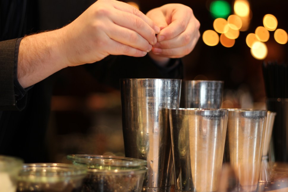 Hands preparing a cocktail over several shakers.