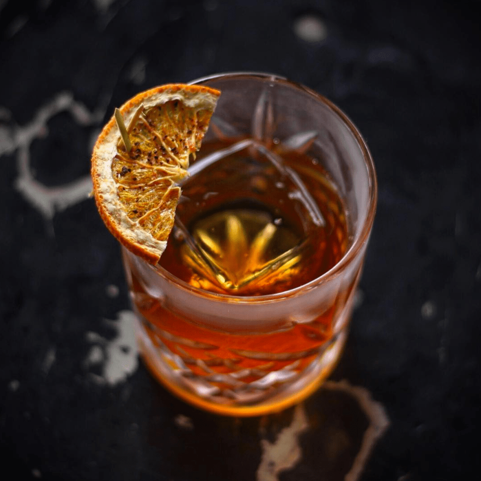 A cocktail with dried citrus garnish on a clear cube at Corner Door in LA.