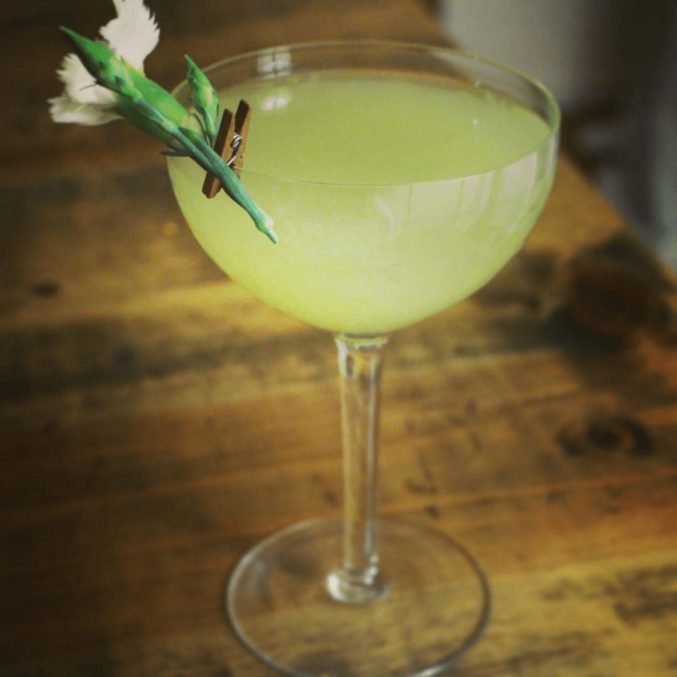 Honeydew cocktail with floral garnish.